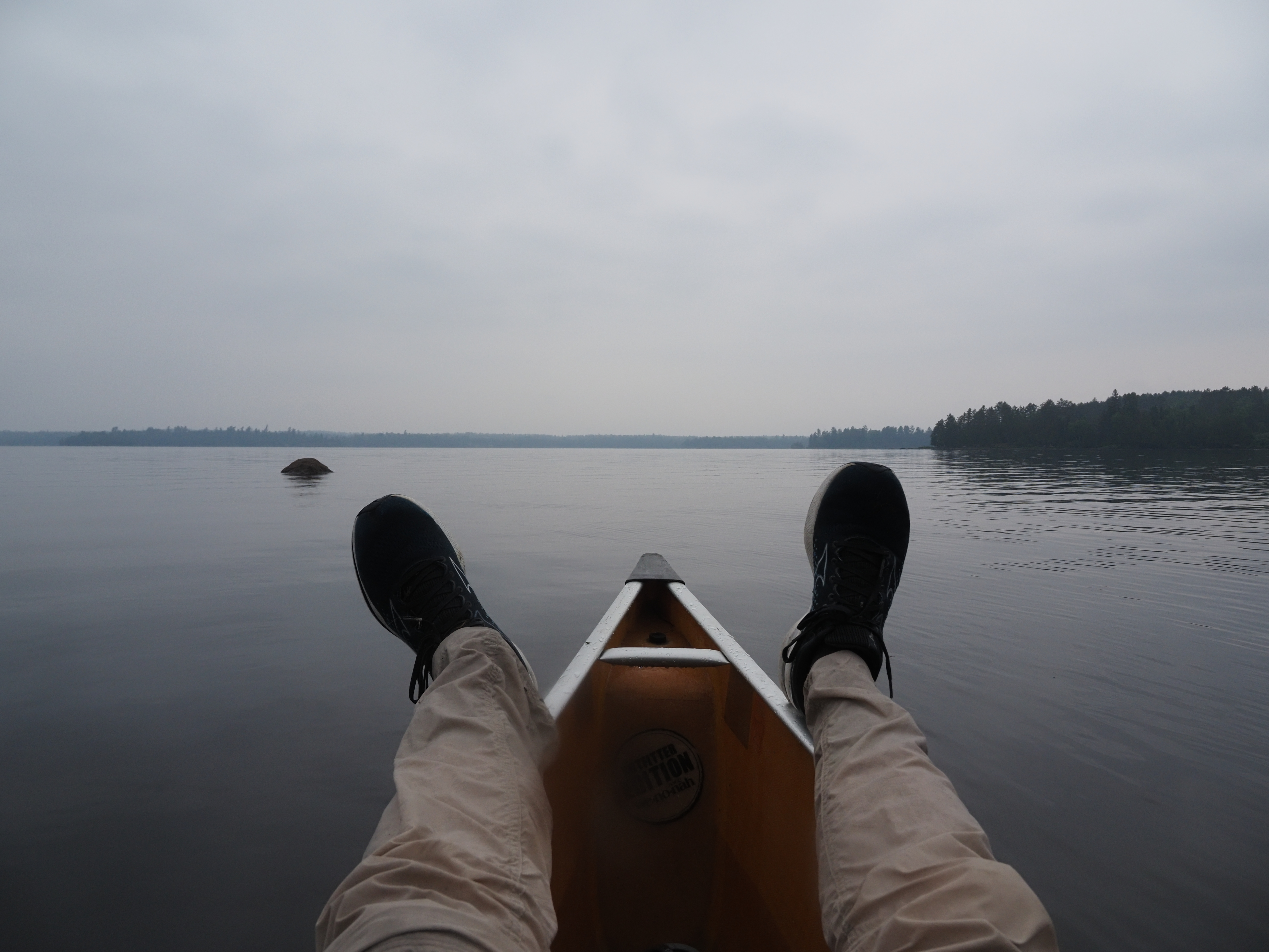 A pair of legs on a canoe on a calm lake