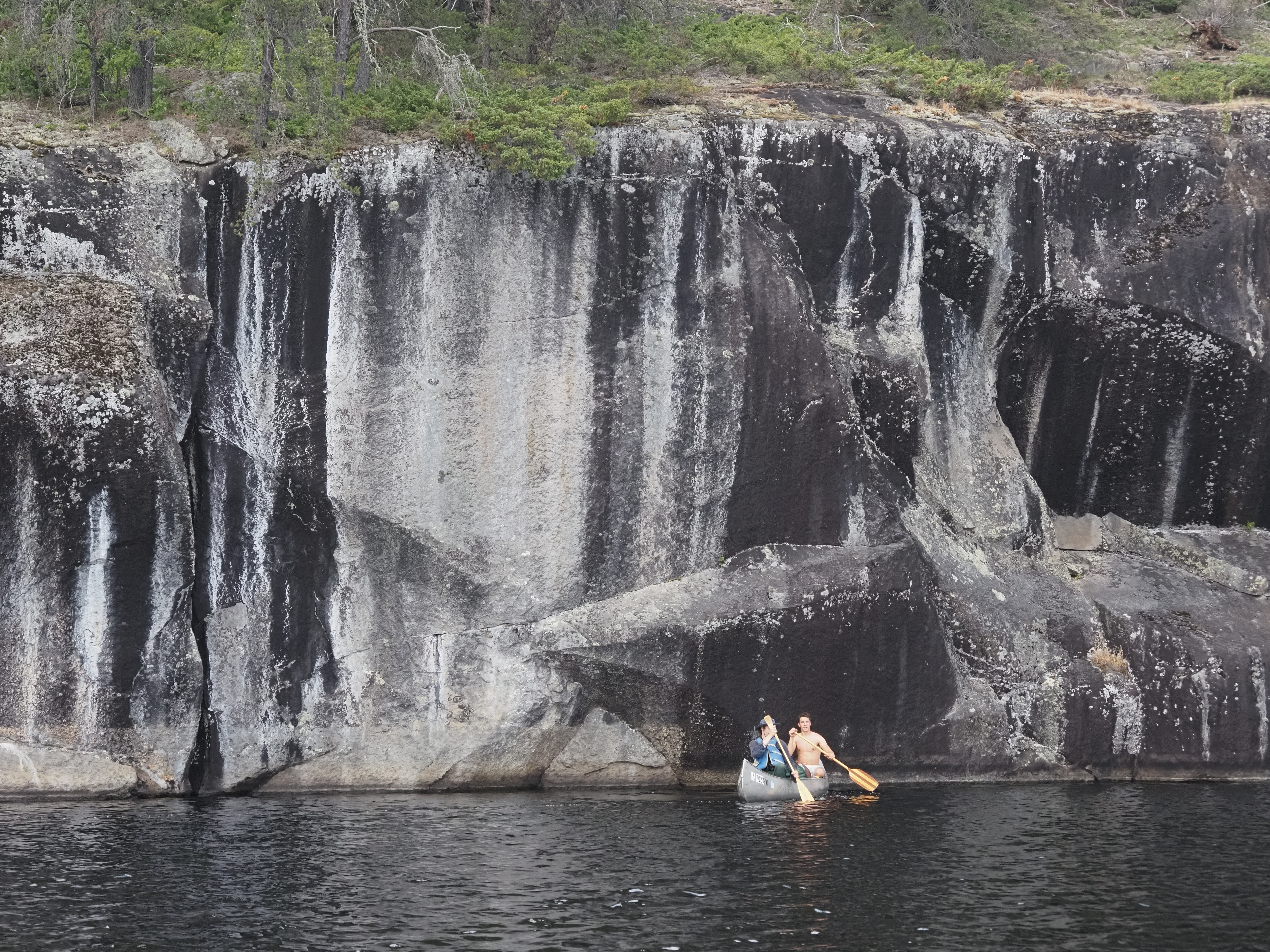 A small canoe in front of a large cliff