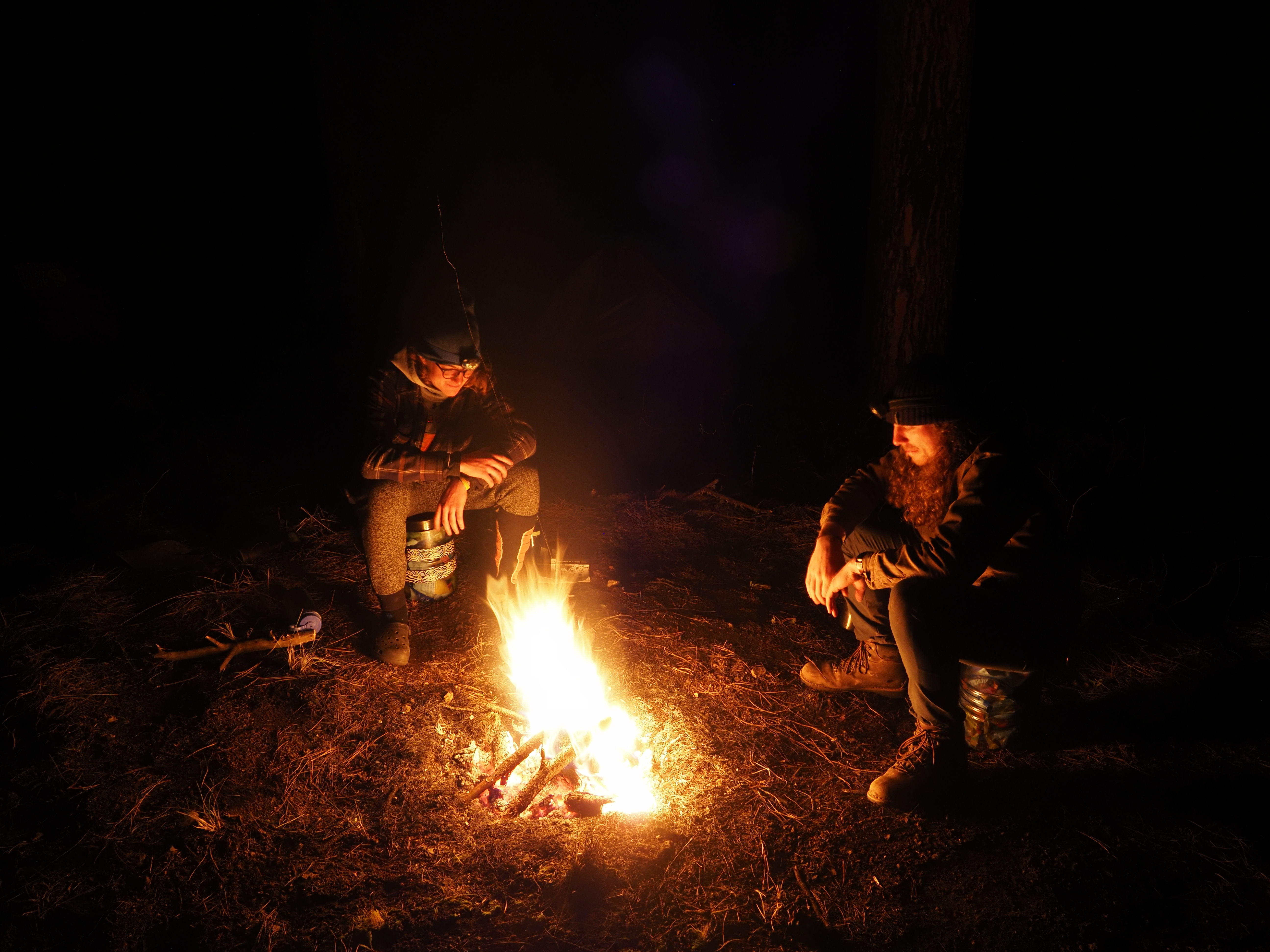 Two people sitting around a campfire at night