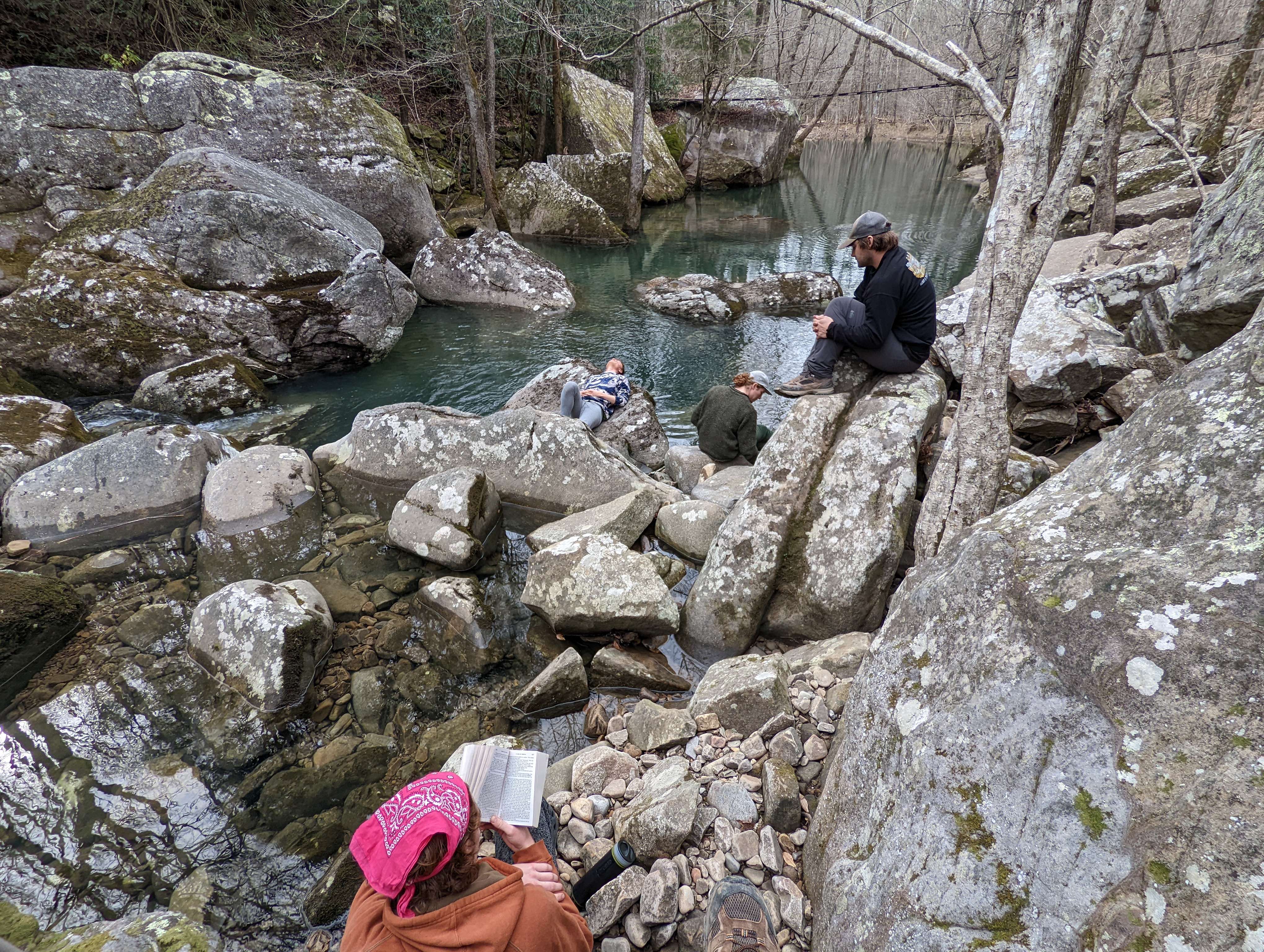 Men laying around on rocks, some of them are reading
